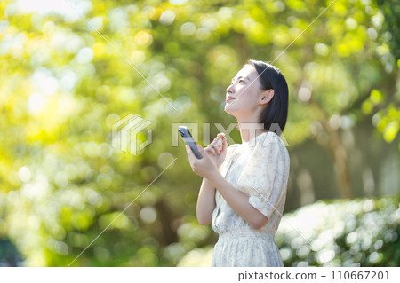 Smiling woman with smartphone among green trees 110667201