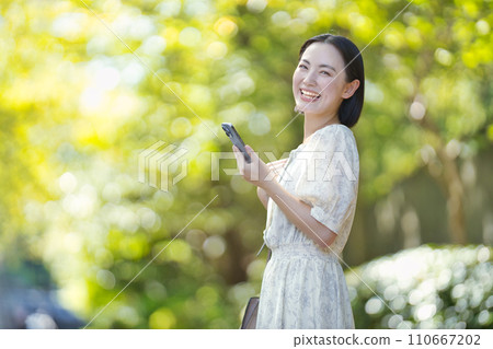 綠樹間帶著智慧型手機的微笑女人 110667202