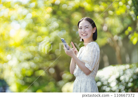 綠樹間帶著智慧型手機的微笑女人 110667372
