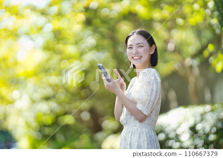 綠樹間帶著智慧型手機的微笑女人 110667379