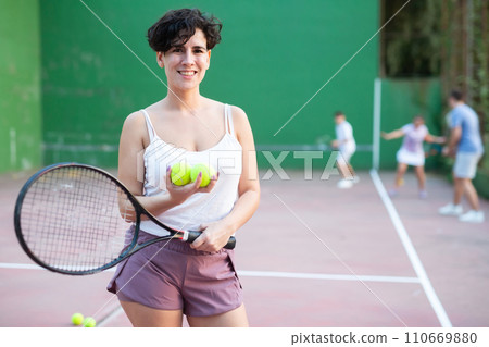 Portrait of latino woman standing on frontenis court, holding racket and ball 110669880