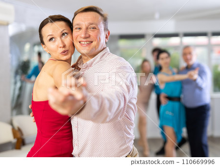 Positive adult couple enjoying slow foxtrot in dance studio 110669996