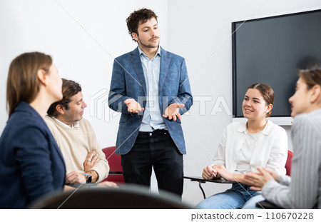 Young male counseling colleagues during psychological training session while they gathered in circle on chairs Young male counseling colleagues during psychological training session while they gathered in circle on chairs 110670228