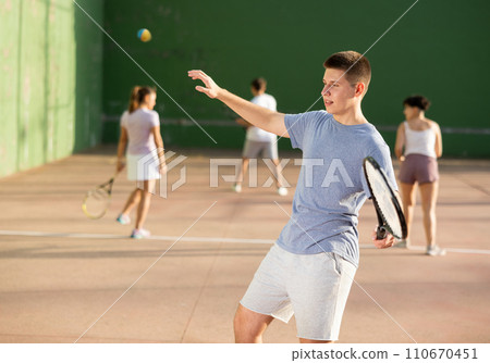Guy hits the ball with a racket while playing frontenis on outdoor court Guy hits the ball with a racket while playing frontenis on outdoor court 110670451