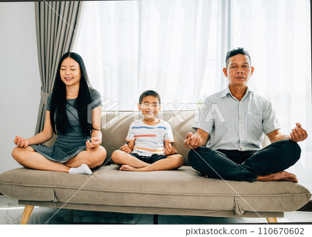 Serene family bonding, parents and their little son practice yoga seated in lotus pose on a sofa. Encouraging harmony balance and tranquility within the home. Serene family bonding, parents and their little son practice yoga seated in lotus pose on a sofa. Encouraging harmony balance and tranquility within the home. 110670602