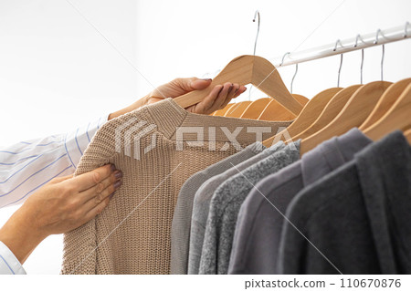 Women's hands choose neutral clothes from a hanger. White, beige and gray jersey. Background. Women's hands choose neutral clothes from a hanger. White, beige and gray jersey. Background. 110670876