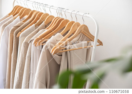 White hanger with beautiful clothes in neutral colors. Monstera flower with large leaves. White hanger with beautiful clothes in neutral colors. Monstera flower with large leaves. 110671038