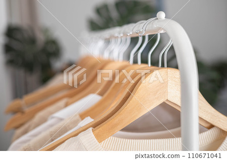 White hanger with beautiful clothes in neutral colors. Monstera flower with large leaves. 110671041