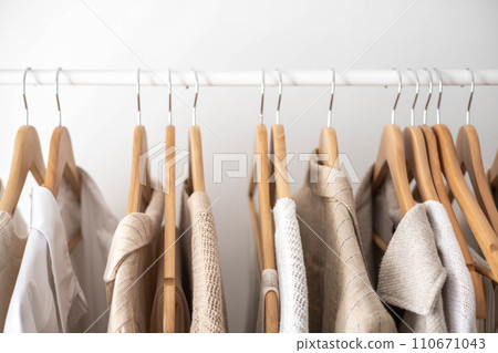 Hanger with neutral beige and white clothes on a white background. 110671043