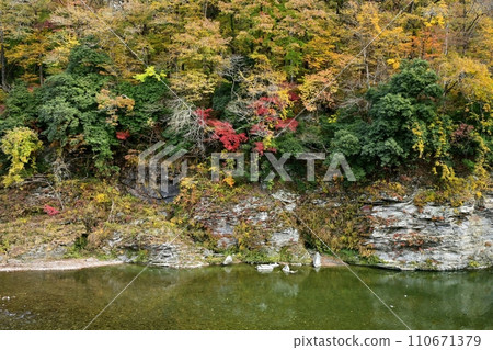 The flow of the Arakawa river and the Chichibu Red Cliffs with autumn leaves above Nagatoro Iwatatami 110671379