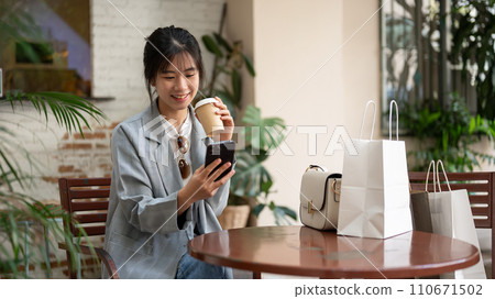 Young beautiful Asian female is using her smartphone and enjoying her coffee while resting in a cafe Young beautiful Asian female is using her smartphone and enjoying her coffee while resting in a cafe 110671502