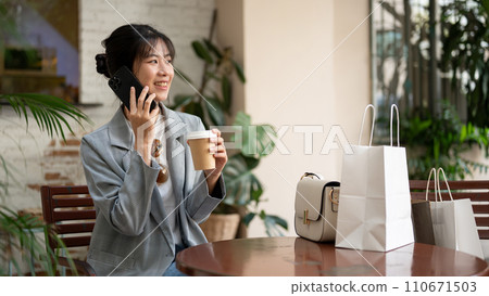 Beautiful Asian woman is talking on the phone with her friend while sitting in a coffee shop. Beautiful Asian woman is talking on the phone with her friend while sitting in a coffee shop. 110671503