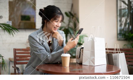 Young beautiful Asian female is using her phone in a cafe after her shopping day in the city. Young beautiful Asian female is using her phone in a cafe after her shopping day in the city. 110671504