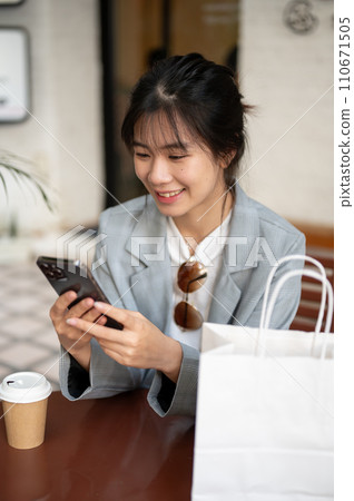 Young beautiful Asian female is using her phone in a cafe after her shopping day in the city. 110671505