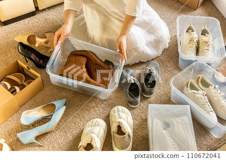 Woman arrangement shoes into plastic container and cardboard box seasonal storage organizing closeup 110672041
