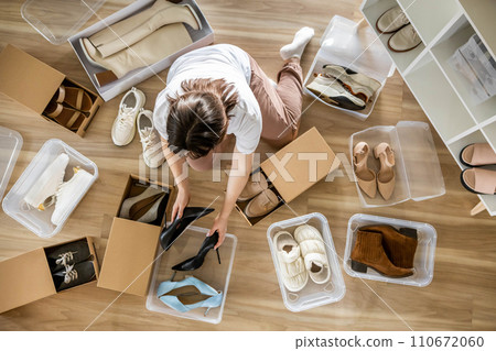 Woman arrangement shoes into plastic container and cardboard box seasonal storage organizing closeup Woman arrangement shoes into plastic container and cardboard box seasonal storage organizing closeup 110672060
