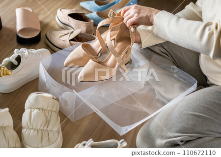 Woman hands packing beige shoes on heels into plastic box for comfortable storage organize top view Woman hands packing beige shoes on heels into plastic box for comfortable storage organize top view 110672110