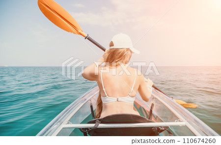 Woman in kayak back view. Happy young woman with long hair floating in transparent kayak on the crystal clear sea. Summer holiday vacation and cheerful female people relaxing having fun on the boat Woman in kayak back view. Happy young woman with long hair floating in transparent kayak on the crystal clear sea. Summer holiday vacation and cheerful female people relaxing having fun on the boat 110674260