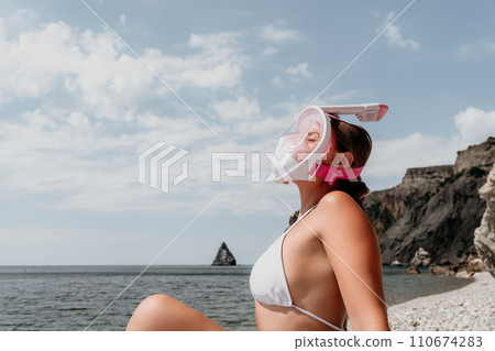 Young happy woman in white bikini and wearing pink mask gets ready for sea snorkeling. Positive smiling woman relaxing and enjoying water activities with family summer travel holidays vacation on sea. 110674283