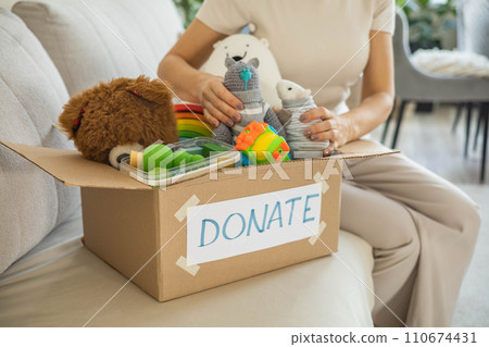 A woman puts toys in a cardboard box for charity. Donation concept. A woman puts toys in a cardboard box for charity. Donation concept. 110674431