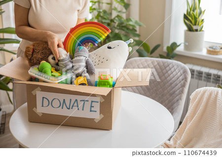 A woman puts toys in a cardboard box for charity. Donation concept. A woman puts toys in a cardboard box for charity. Donation concept. 110674439