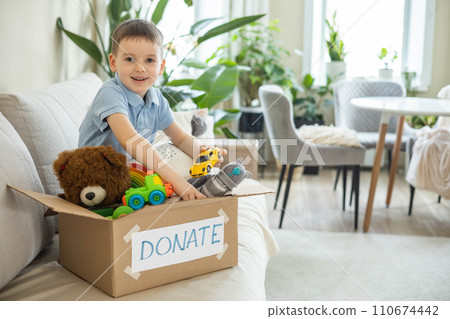 Boy child puts toys in a cardboard box for charity. Donation concept. Boy child puts toys in a cardboard box for charity. Donation concept. 110674442
