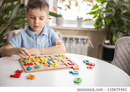 A Caucasian light-haired boy of five years old with blue eyes is putting together a puzzle  110674462