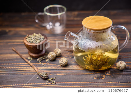 Teapot and glass cup with blooming tea flower inside on a wooden table 110676627