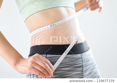 A woman measuring her stomach circumference with a tape measure 110677159