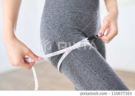A woman measuring the circumference of her thighs with a measuring tape 110677163