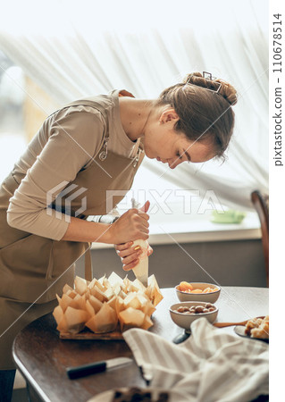 young woman applies cream to cupcakes in craft paper. the concept of food delivery. a birthday package. small business. bakery chef bakes cakes in kitchen young woman applies cream to cupcakes in craft paper. the concept of food delivery. a birthday package. small business. bakery chef bakes cakes in kitchen 110678514