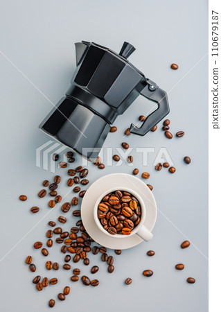 Bialetti moka pot. Coffee maker and coffee beans in mug on gray background. Top view. Bialetti moka pot. Coffee maker and coffee beans in mug on gray background. Top view. 110679187
