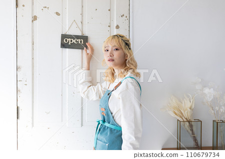 A young woman hanging an opening plate on the door of a store 110679734