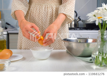 Woman separates yolk and white over bowl on kitchen preparing food at home. 110681276