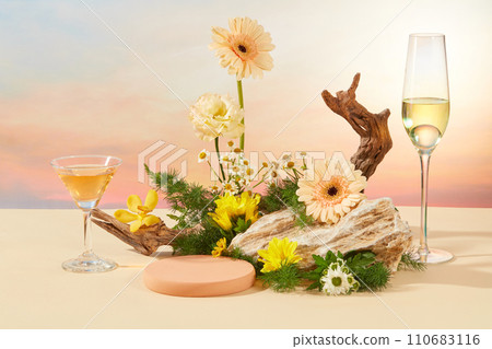 A cocktail and a glass of wine are displayed alongside fresh flowers, grass and stone slabs. An empty platform is placed in the center for the display with a sunset view. 110683116