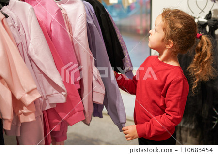 Cute child girl chooses sweater in shopping mall with clothes 110683454