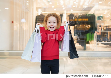 Happy child girl in red sweater with shopping bags in cloth store. Black Friday concept 110683456
