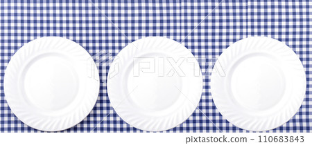 White Plates on Blue and White checkered Fabric Tablecloth Background White Plates on Blue and White checkered Fabric Tablecloth Background 110683843
