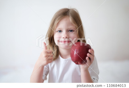 Smiling girl holding thumbs up and holding ripe apple Smiling girl holding thumbs up and holding ripe apple 110684013
