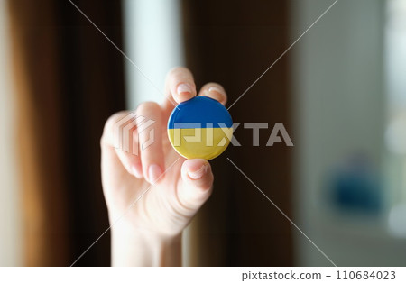 Person holds round badge Flag of Ukraine closeup 110684023