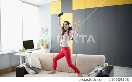Happy woman dancing on couch, listen to music in headset and sing 110684198