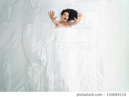 Pretty woman laying on white bedding, wake up well rested in morning, stretching after sleep 110684219
