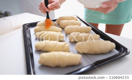 Woman prepares croissants and brush dough with egg yolk Woman prepares croissants and brush dough with egg yolk 110684233