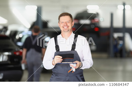 Smiling maintenance center worker in uniform, man fill in papers on car checkup 110684347