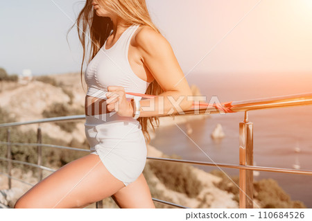 Fitness woman sea. Outdoor workout with fitness rubber bands in park over beach. Female fitness yoga routine concept. Healthy lifestyle. Happy fit woman exercising with rubber band in park. 110684526