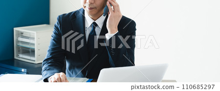 Businessman talking on smartphone while looking at computer Businessman talking on smartphone while looking at computer 110685297