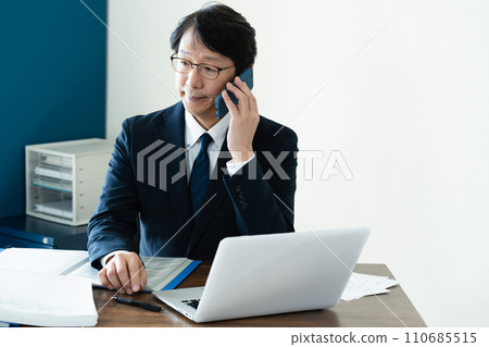 Businessman talking on smartphone while looking at computer Businessman talking on smartphone while looking at computer 110685515