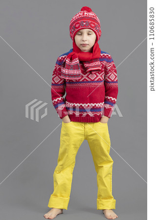 A child in warm clothes. Boy in a winter hat, scarf and red sweater barefoot. Fashionable boy in the studio. A child in warm clothes. Boy in a winter hat, scarf and red sweater barefoot. Fashionable boy in the studio. 110685830
