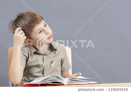 The child at the table is doing homework. Primary school student at a desk with a textbook. The child at the table is doing homework. Primary school student at a desk with a textbook. 110685839