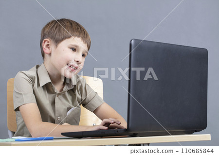 The child at the laptop. The boy looks at the monitor screen. Preschooler at the computer. Junior student at a table with a computer. The child at the laptop. The boy looks at the monitor screen. Preschooler at the computer. Junior student at a table with a computer. 110685844